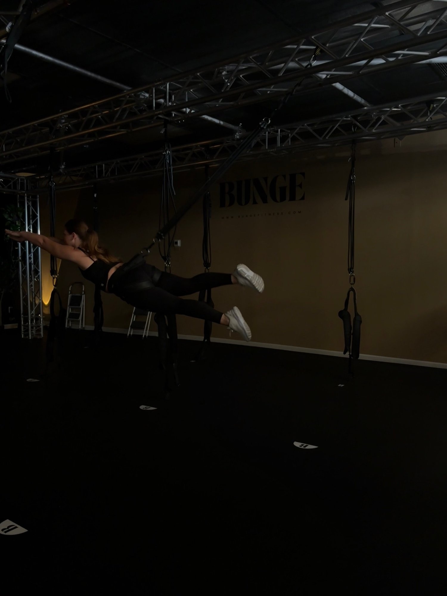 A student holding a flying arabesque pose on the bungee cord in front of the BUNGE logo wall in Huntington Beach
